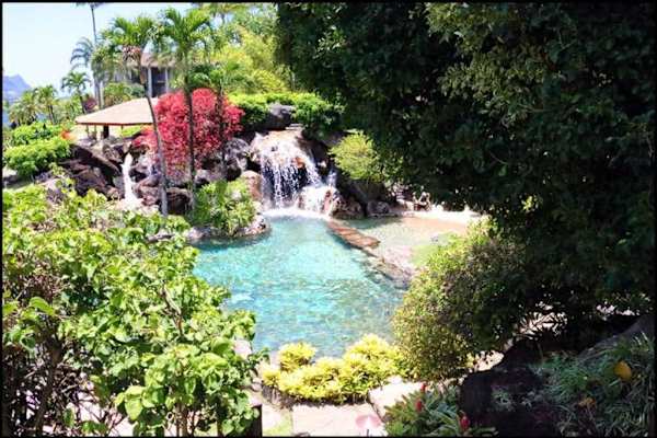 Waterfall flows through lush greenery, rocks, and peaceful landscaping