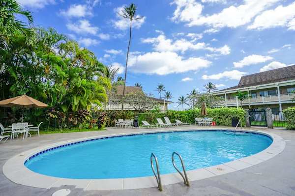 Resort outdoor swimming pool with sun loungers, umbrella seating & palm trees