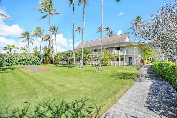 Paved pathway leading past manicured lawn and palm trees