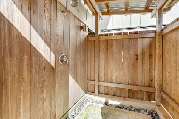 Outdoor shower area features wood fencing, pebbles, and natural light
