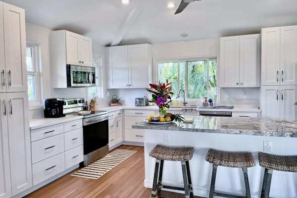 Fully equipped kitchen with white cabinetry, island barstools, and garden views