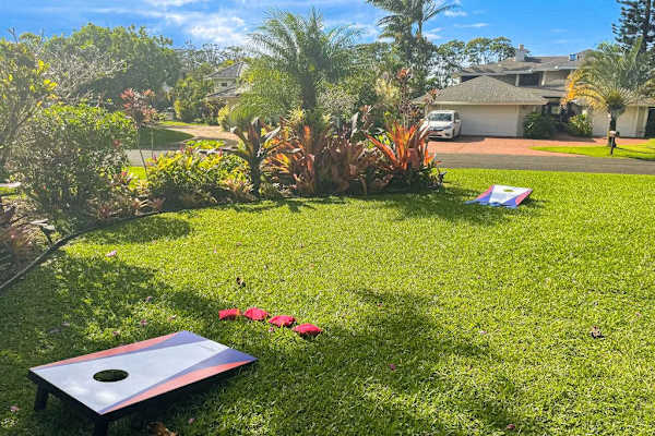 Spacious green lawn with cornhole boards & tropical landscaping