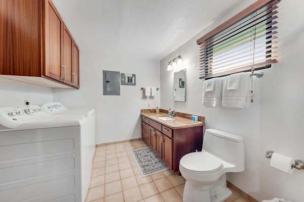 Washer and dryer sit beside bright vanity and tiled bath