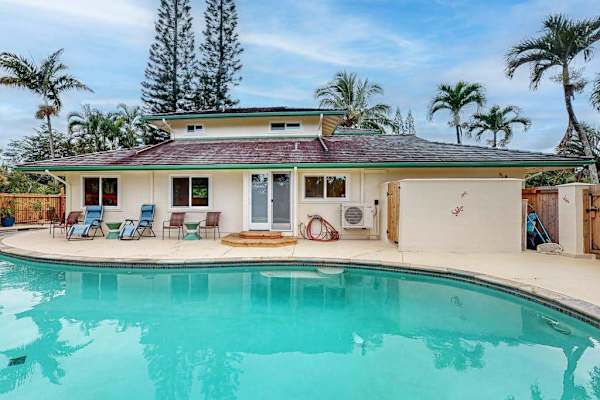 Pool glistens beside palms with home facade and tropical sky