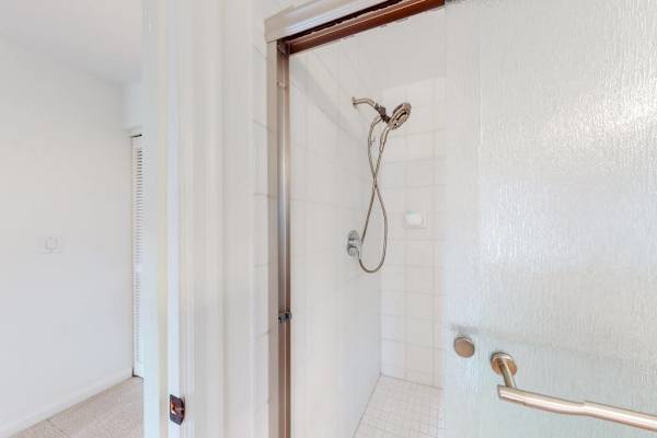 Shower features handheld fixture, grab bar, and clean tiled walls