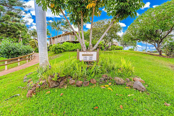 Landscaped property entrance features lush grass tropical plants and signage