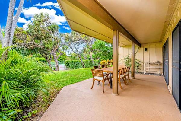 Shaded exterior walkway provides seating beside lush tropical landscaping outdoors