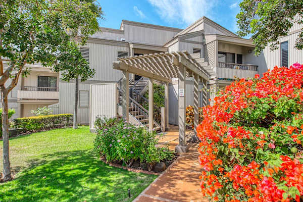 Two-Story Condo Exterior with Wooden Pergola Entryway and Lush Tropical Flowers