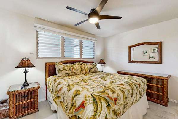 First bedroom features king bed botanical quilt nightstands and fan