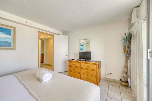 Bright and spacious bedroom with a TV, dresser, and peaceful island-inspired décor for a restful stay.