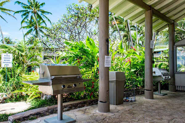 Covered BBQ area features grill counter and tropical garden surroundings