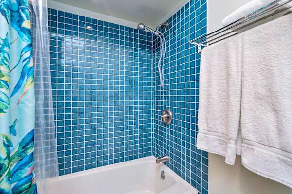 Tiled shower area includes glass doors fixtures and hanging towels