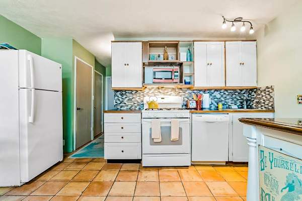 Bright kitchen showcases white cabinetry, refrigerator, patterned backsplash, and island