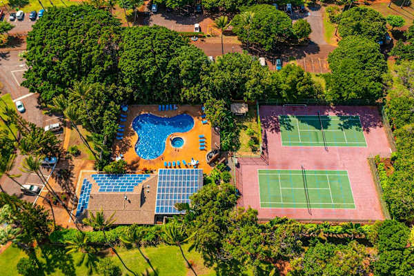 Aerial view highlights swimming pool, tennis court, gardens, and homes