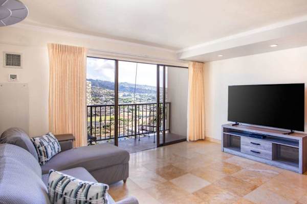 Bright open-concept living room with a private balcony, Smart TV, and panoramic city and mountain views.