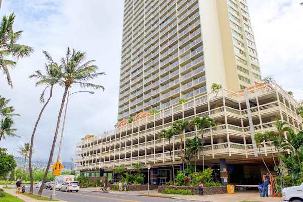 Welcome to your tropical getaway at this towering high-rise building, featuring a convenient multi-level parking garage and an inviting street-level entrance lined with palm trees.