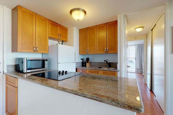 The convenient cooking area includes a flat-top electric stove and a microwave, seamlessly connecting to a hallway that leads through the unit.