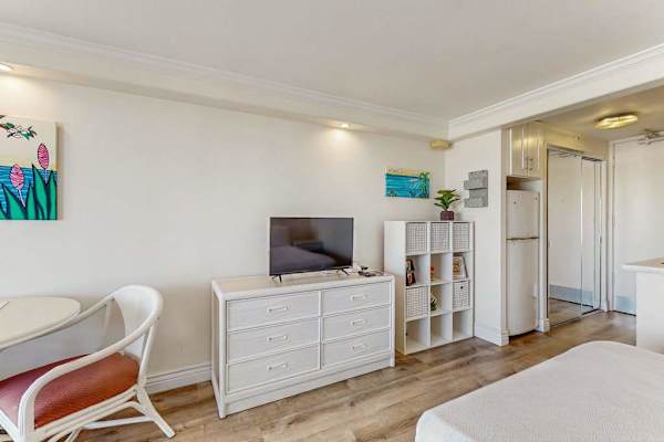 The studio layout features a flat-screen TV on a white dresser, versatile cube storage, and sleek wood-style flooring.
