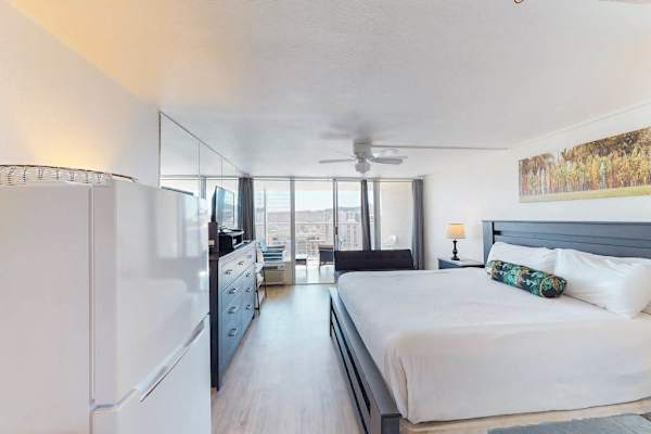 Bright studio floor plan with light flooring, a king bed setup, and floor-to-ceiling glass sliding doors opening to the balcony.