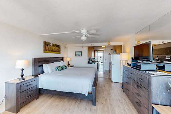 This open-concept studio offers a plush bed, ceiling fan, and flat-screen TV in a bright and inviting layout.