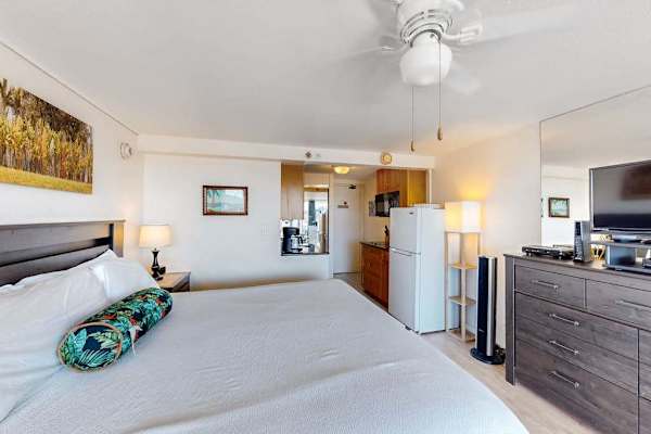 This studio layout seamlessly combines a comfortable sleeping area with a full dresser, flat-screen TV, and easy access to the kitchenette.