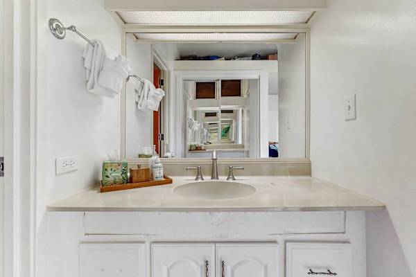 Vanity displays mirror, sink, toiletries, towels, and bright cabinetry