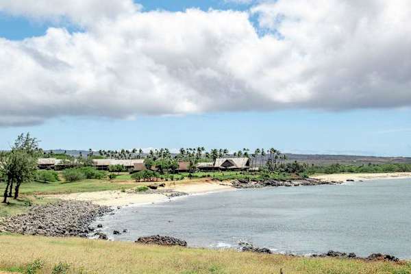 Nearby coastline shows calm water, rocky shore, lawns, and clouds