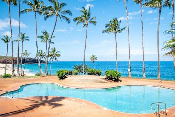 Resort pool invites swimming beside palms, ocean, and tropical gardens