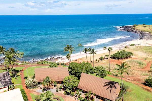 Aerial scene shows resort roofs, trees, pool, beach, and ocean