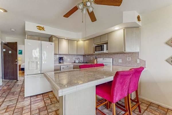 Kitchen island anchors pink stools, appliances, counters, and upper cabinets