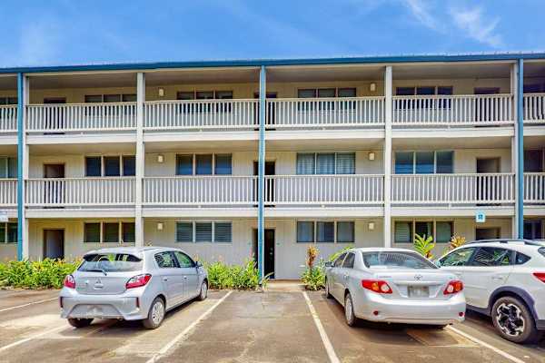 Resort building displays balconies, palm landscaping, parking spaces, and skies