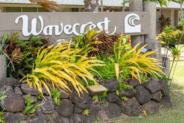 Wavecrest entrance sign sits among volcanic rocks and tropical plants