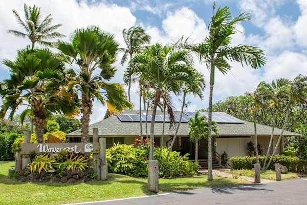 Resort entrance welcomes guests with palms, parking, low buildings, and sunshine