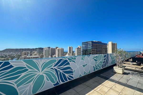 Rooftop pool edge framed by Waikiki skyline and tropical mural
