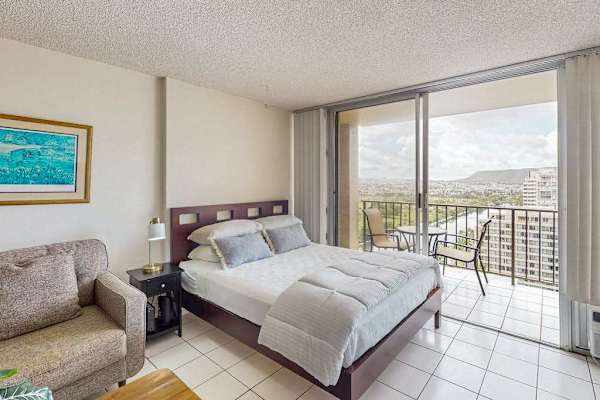Queen bed and sofa beside bright balcony doors