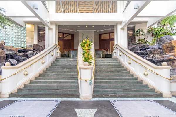 Arrive in style at the iconic Ilikai Hotel entrance, where grand, sweeping staircases and lush tropical accents welcome you to the ultimate Hawaiian getaway.