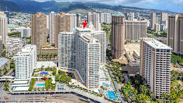 A stunning aerial view showcasing the Ilikai Hotel in the heart of Waikiki, highlighted against the city skyline and lush mountains.