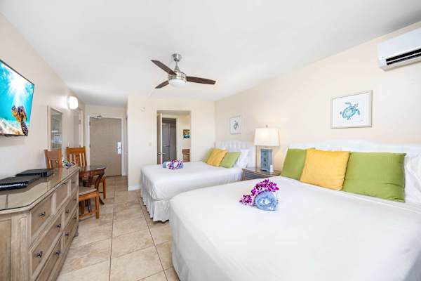 The unit features two queen-size beds, a 42" Samsung TV, split air-conditioning and a ceiling fan, a dresser and nightstand, direct access to a bathroom with a walk-in shower, and private lanai (balcony) access.