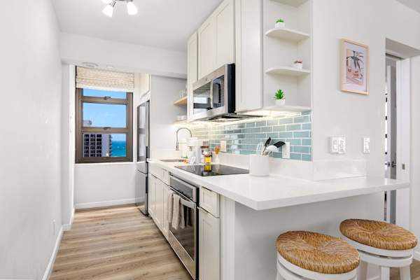 Sleek galley kitchen w/ modern appliances, tile backsplash & window views