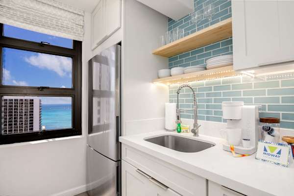 Kitchen sink area w/ blue tile backsplash & window letting in natural light