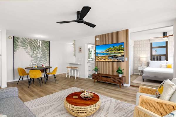 Open living & dining area w/ cozy seating, round table & TV wall dividing the bedroom space