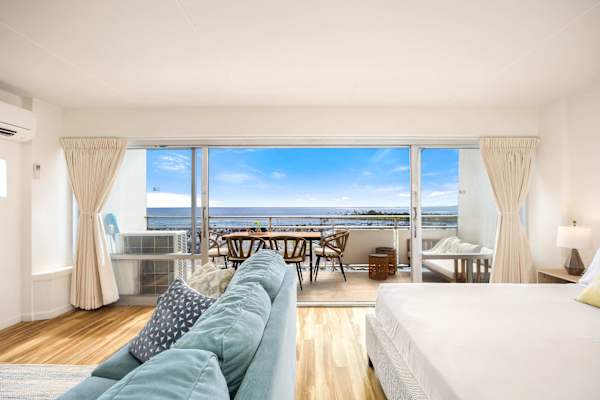 This bright, open-plan studio perfectly blends comfort and luxury, featuring an inviting living area with a plush teal sofa and a king-size bed
