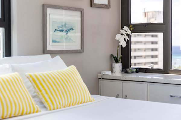 Bright bedroom corner with striped yellow pillows and a view through the window.