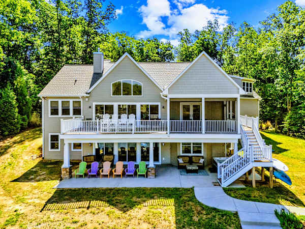 Rear Exterior - The lake-facing side opens across two deck levels, a screened porch, and a patio lined with bright Adirondack chairs.