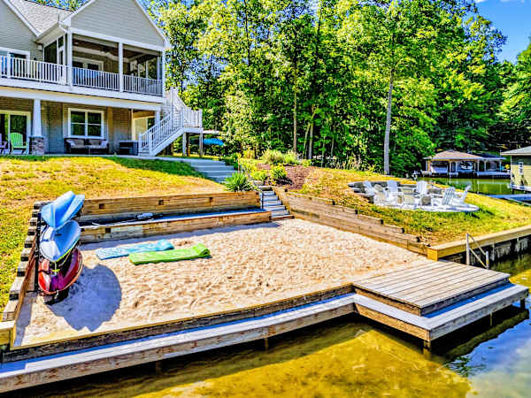 Sandy Beach - A rare flat, sandy shoreline with kayaks waiting at the water's edge and terraced lawn stepping down from the house.
