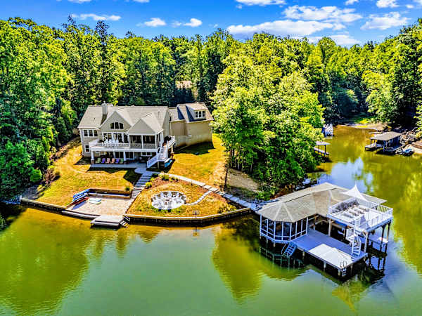 Aerial View - The full lakefront setup at a glance: open lawn, fire pit, sandy beach, dock, and boathouse steps from the back door.