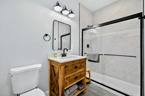 Lower Bathroom - A reclaimed-wood vanity with quartz counter and black fixtures pairs with a glass-enclosed shower wrapped in soft marble-look tile.