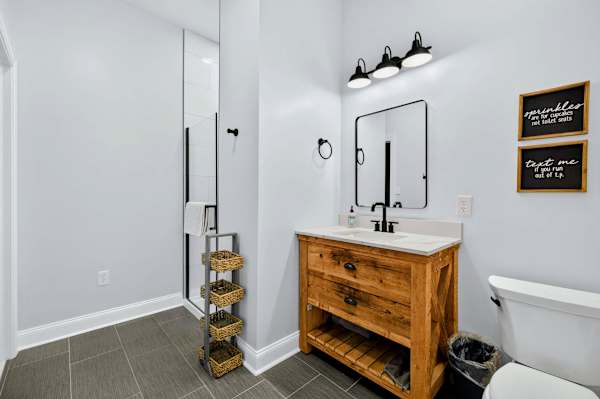 Bunk Bathroom - A reclaimed-wood vanity and quartz counter, black fixtures, and a basket ladder stacked with towels bring warm farmhouse character to this full bath.