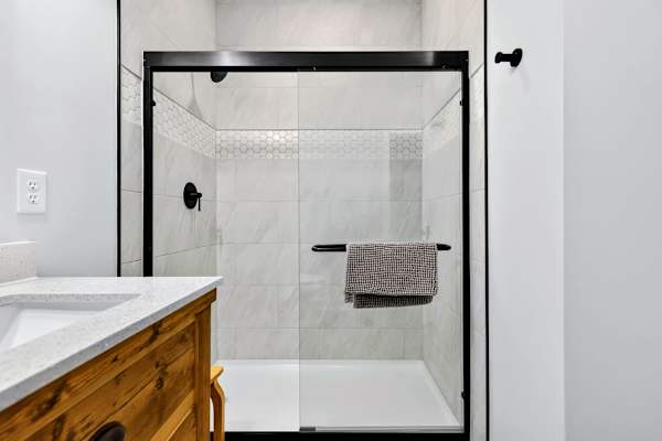 Lower Bathroom - The walk-in glass shower is finished in marble-look tile with a hexagon accent band and matte black fixtures, clean and spa-like.
