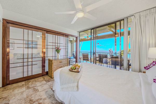 Comfortable bed setup featuring a cooling ceiling fan and a beautiful ocean view. 🛏️